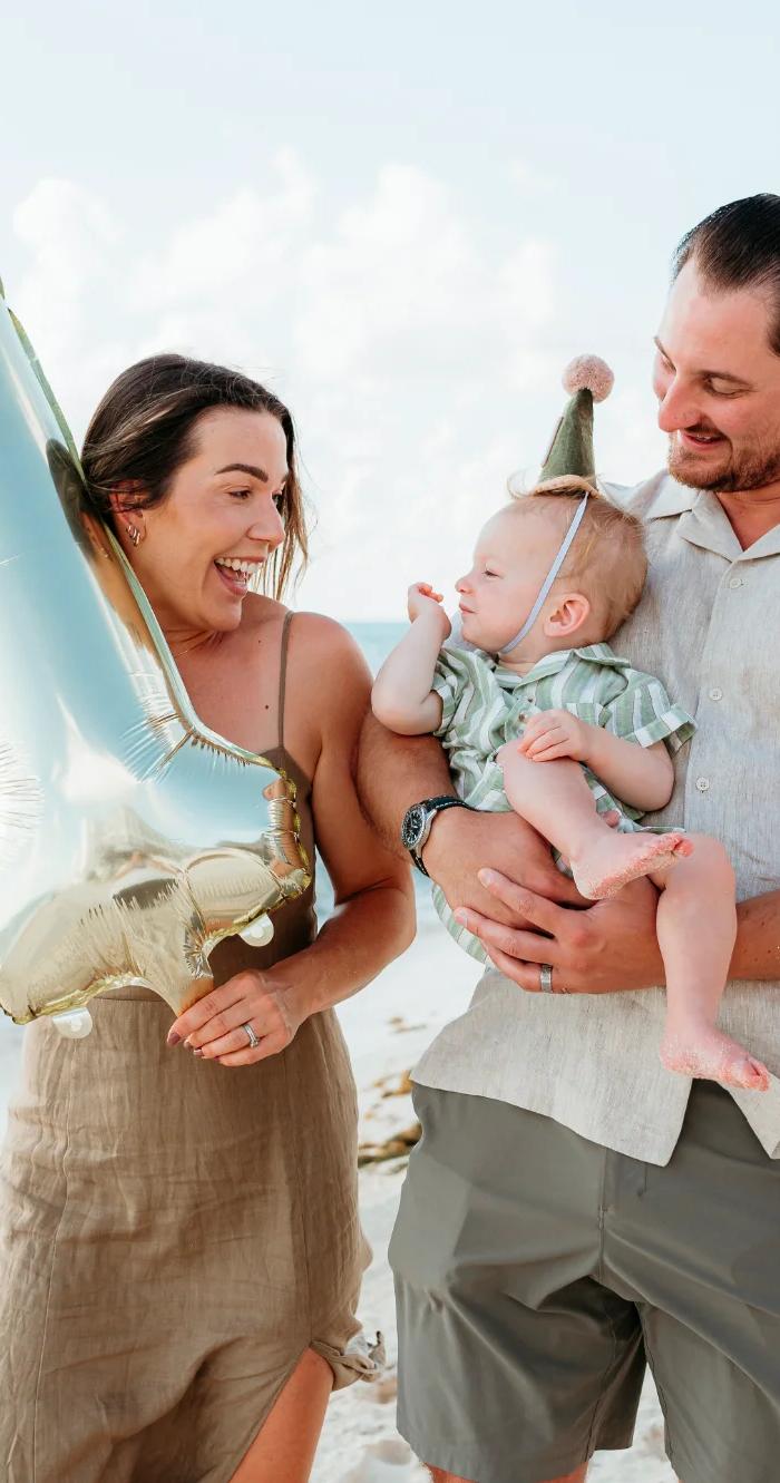 Parents on the beach with their baby and a number one balloon for a first birthday